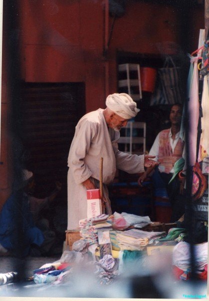 An elderly man calls by at a merchant's stall