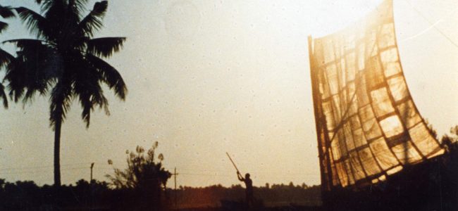 Cargo boat on Kerala canals, India, the sail made of sacks stitched together is lit through by a lowering sun