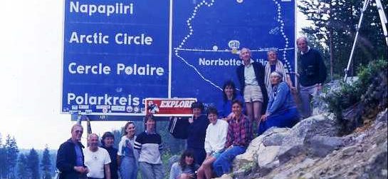 Swimmers posing by the Arctic Circle sign in Sweden - a lake lies across the invisible line