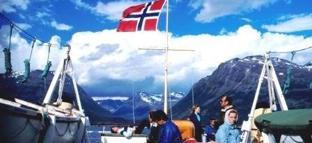 A view over the rear of a ferry in north Norway, mountains rise steeply toward clear skies